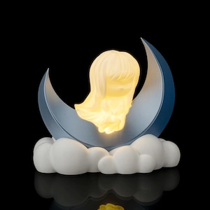 May include: A night light shaped like a girl sitting on a crescent moon. The girl and moon glow with a soft yellow light. The moon is blue and rests on a bed of white clouds. The background is black.