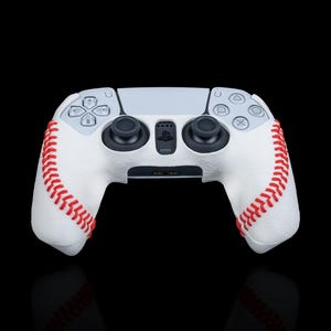 May include: A white PlayStation 5 DualSense controller with a baseball-stitched grip. The controller has red stitching and a white base.