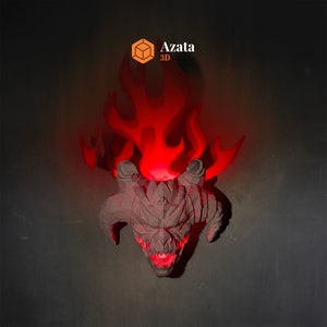 May include: A 3D printed demon head sculpture with horns and a menacing expression. The sculpture is lit from behind with red light, creating a fiery effect. The sculpture is labelled "Azata 3D".