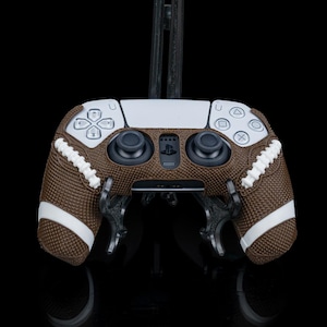 Könnte beinhalten: Eine braune und weiße Controller-Haut im Football-Design für einen Playstation 5-Controller. Die Haut hat eine braune Ledertextur mit weißen Nähten und Schnürsenkeln.