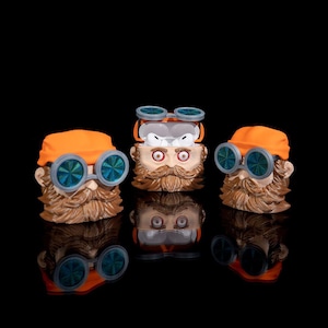 Puede incluir: Tres estuches para AirPod de color naranja y marrón con una cara de dibujos animados, gafas y bigote. Los estuches están abiertos y los auriculares AirPod son visibles en el interior.