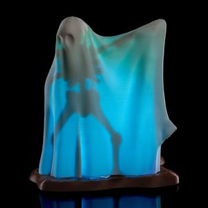May include: A blue and white ghost figurine with a glowing light inside. The ghost is standing on a brown base.