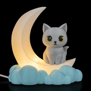 May include: A gray cat figurine with yellow eyes sits on a white crescent moon, atop blue cloud-shaped base. The moon glows with a soft light, creating a whimsical night light. The background is black.