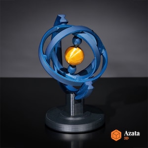 May include: A blue 3D printed sculpture of a sphere with a smaller sphere inside. The outer sphere is made of multiple rings that intersect each other. The inner sphere is a golden color. The sculpture is on a black base.