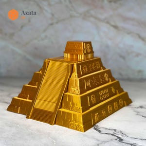 May include: A gold-coloured model of a Mayan pyramid with intricate carvings and a small temple on top. The pyramid is made of multiple layers and has a staircase leading up to the temple.