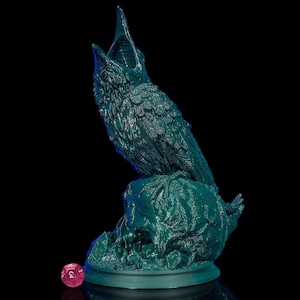 May include: A teal green 3D printed figurine of a bird with its beak open, perched on a rock. The bird is detailed with feathers and has a textured surface. A small red dice is in the foreground.
