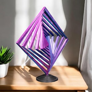 May include: A purple and blue geometric wooden sculpture with a black base. The sculpture is made of multiple layers of wood that are stacked on top of each other to create a 3D effect.