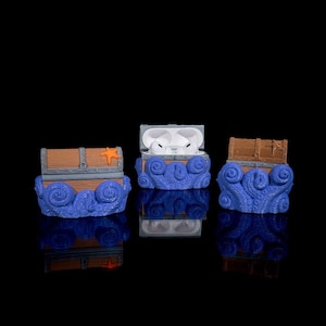 Puede incluir: Tres estuches para Airpods impresos en 3D con forma de cofres del tesoro con un diseño de olas azules. El estuche del medio está abierto, revelando los Airpods blancos en el interior.