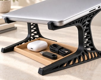 May include: A black laptop stand with a complex, lattice-like structural design supports a silver laptop. Beneath the laptop, a tan rectangular tray holds a white wireless earbud case, a black USB flash drive, and a coiled black charging cable.