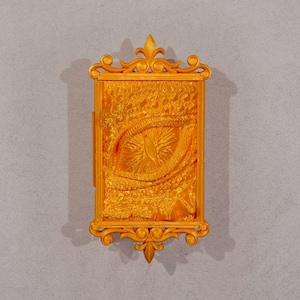 May include: A gold-coloured decorative wall plaque with an ornate frame and a raised image of a dragon's eye.