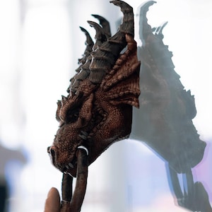 May include: A brown dragon head door knocker with a ring handle. The knocker is mounted on a white wall.