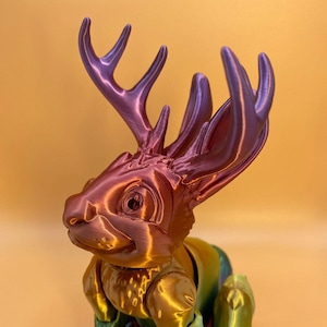 Può includere: Una statuetta stampata in 3D di un cervo con la testa di un coniglio, con una finitura dorata e viola metallica iridescente.
