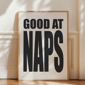 May include: A framed poster with the text "GOOD AT NAPS" in black bold letters on a white background.