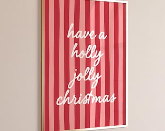May include: A rectangular wall art print in a thin gold frame featuring vertical stripes in alternating shades of red and pink. The center of the print displays the white handwritten-style text that reads, have a holly jolly christmas.