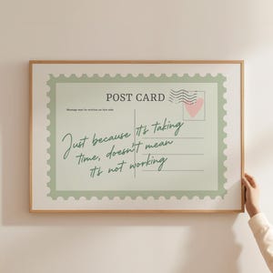 Puede incluir: Impresión enmarcada de postal con fondo verde claro y diseño de sello postal. El texto dice: "Solo porque lleva tiempo, no significa que no funcione". Un corazón rosa está en el sello.