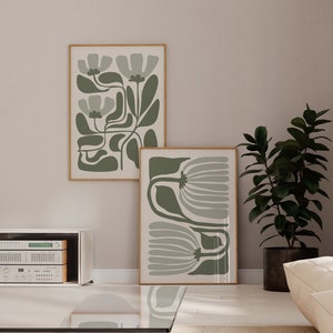 Peut inclure: Deux impressions d'art abstrait encadrées avec un motif floral vert et blanc. Les impressions sont accrochées à un mur beige clair. Une plante verte en pot se trouve dans le coin de la pièce.