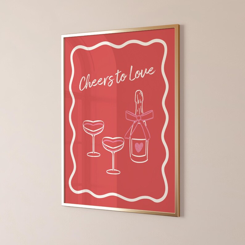 K&ouml;nnte beinhalten: Ein roter gerahmter Druck mit einem wei&szlig;en Rahmen und dem Text "Cheers to Love" in wei&szlig;er Schrift. Der Druck zeigt eine rosafarbene Champagnerflasche mit einer rosafarbenen Schleife und zwei rosafarbene Champagnergl&auml;ser.