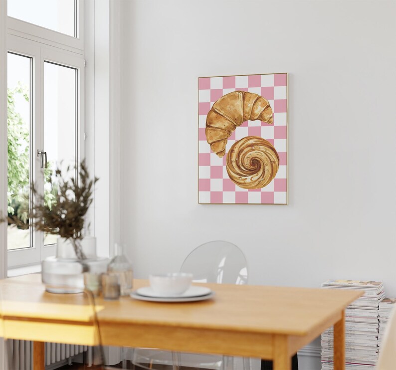 K&ouml;nnte beinhalten: Ein Aquarellbild eines Croissants und eines Zimtschnecken auf einem rosa-wei&szlig; karierten Hintergrund.
