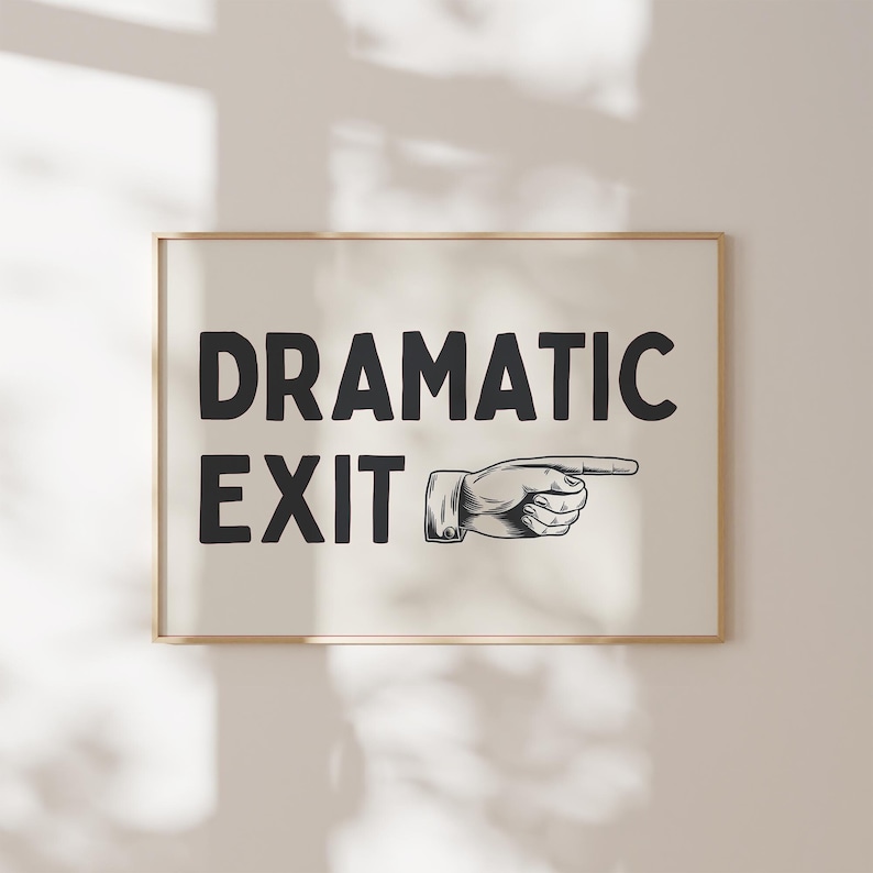 May include: A black and white print with the text "Dramatic Exit" and a pointing hand graphic. The print is framed in a light wood frame.