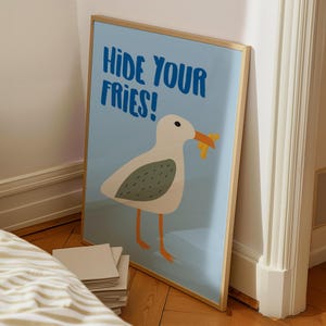 May include: A blue and white framed poster with a cartoon seagull holding a french fry in its beak. The poster says "Hide Your Fries!" in blue text.