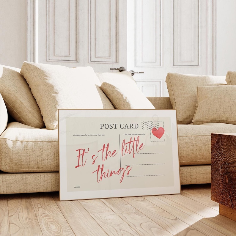 Pu&ograve; includere: Una stampa incorniciata di cartolina con la scritta "It's the little things" in un carattere corsivo. Il design della cartolina include un timbro a forma di cuore rosso e le parole "Post Card" in alto. La stampa &egrave; esposta su un pavimento in legno davanti a un divano beige.