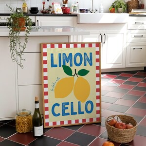 May include: A framed print with a red and white checkered border. The print features a yellow background with the text "LIMON la dolce vita CELLO" in blue and white. Two yellow lemons with green leaves are depicted on the print.
