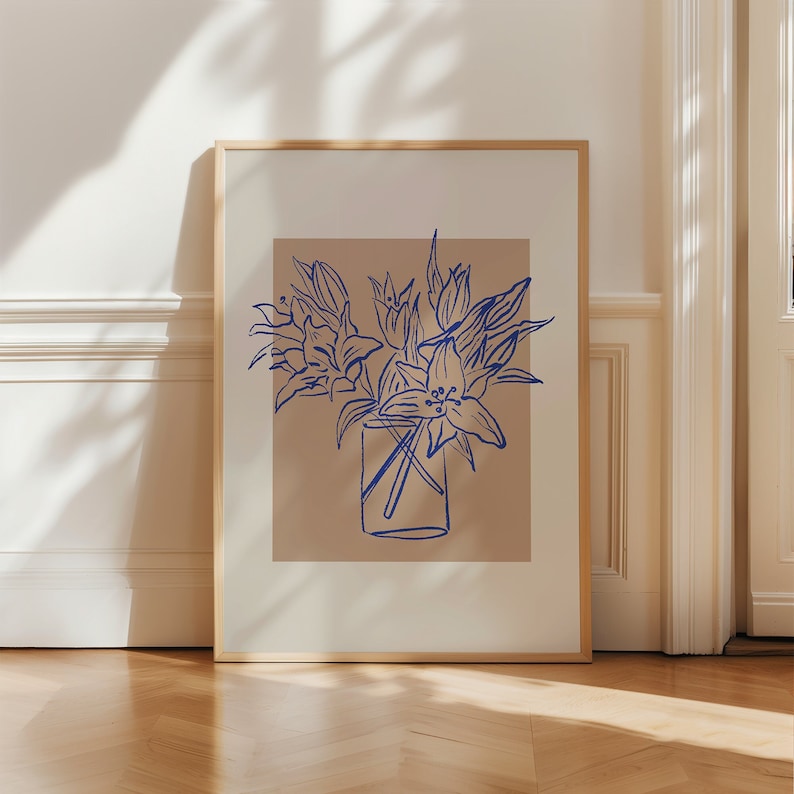 May include: A framed print of a blue line drawing of a bouquet of lilies in a glass vase on a light brown background.