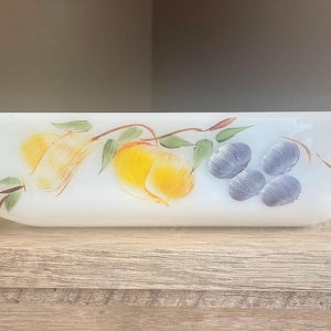 May include: White rectangular baking dish with hand-painted fruit design. The dish features yellow pears, yellow and orange peaches, and purple plums with green leaves. The dish has curved handles on each end.