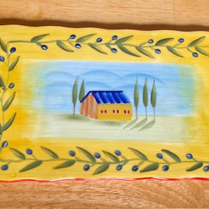 May include: Rectangular ceramic serving platter with a hand-painted design. The yellow border features olive branches and blue olives. The center depicts a house with a blue roof and trees against a blue and yellow sky.