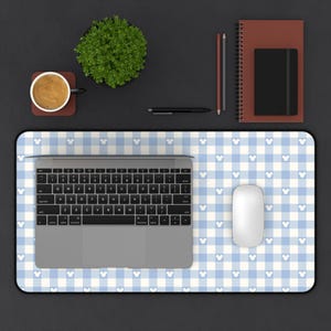 May include: A computer desk setup featuring a blue and white checkered mousepad with Mickey Mouse head icons. A laptop, white mouse, and other office supplies are on the desk. A cup of coffee, a small plant, and a notebook are also visible.