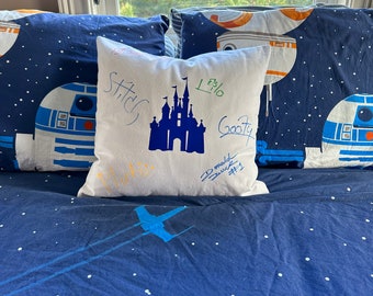 Puede incluir: Una almohada blanca con una silueta azul del castillo de Cenicienta y el texto "Stitch", "L3/16", "Goofy" y "Donald Duck" escrito en ella. La almohada está sobre una colcha azul con estrellas blancas y un X-wing azul.
