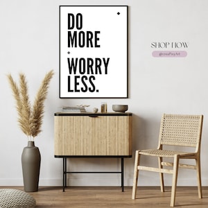Könnte beinhalten: Ein schwarz-weißer druckbarer Wandkunstdruck mit dem Text "DO MORE WORRY LESS." Der Druck ist gerahmt und hängt an einer weißen Wand über einem Holzkasten. Der Text ist in einer fetten, serifenlosen Schriftart. Der Druck ist Teil einer Wohnkultur-Kollektion.