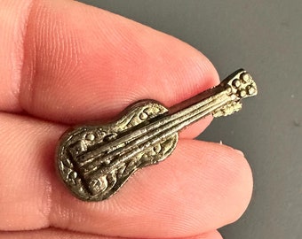 Puede incluir: Un pin de guitarra de metal dorado con detalles intrincados. El pin es pequeño y delicado, perfecto para agregar un toque de música a tu ropa o bolso.