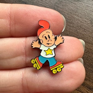 Puede incluir: Un pin de esmalte con un personaje de dibujos animados en patines. El personaje lleva un sombrero rojo, una camisa blanca con una estrella amarilla, pantalones azules y patines rojos con ruedas amarillas.