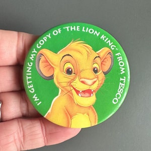 Puede incluir: Botón verde con una imagen de dibujos animados de Simba de El Rey León. El texto en el botón dice "Estoy consiguiendo mi copia de "El Rey León" de Tesco."