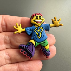 Puede incluir: Una figura de dibujos animados amarilla, azul, roja, verde y morada sobre patines. La figura lleva un sombrero rojo y una camisa azul con una Y amarilla en ella. La figura sonríe y tiene los brazos extendidos.