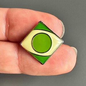 May include: A diamond-shaped pin featuring the Brazilian flag design. The pin has a green border, a yellow diamond shape, and a green circle in the center. The pin is made of metal and enamel.