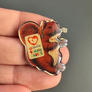 May include: A gold-colored metal pin featuring a cartoon squirrel holding a tag that reads "Ty Teenie Beanie Babies".