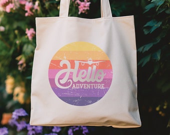 May include: A white canvas tote bag with a colorful circle design. The circle has a rainbow gradient with a white airplane and the text "Hello Adventure".