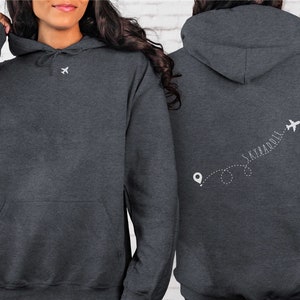 May include: A dark gray hoodie with a white airplane and the text "SKY&ADDLE" on the back. The text is written in a cursive font and is followed by a dotted line with a small airplane icon at the end.