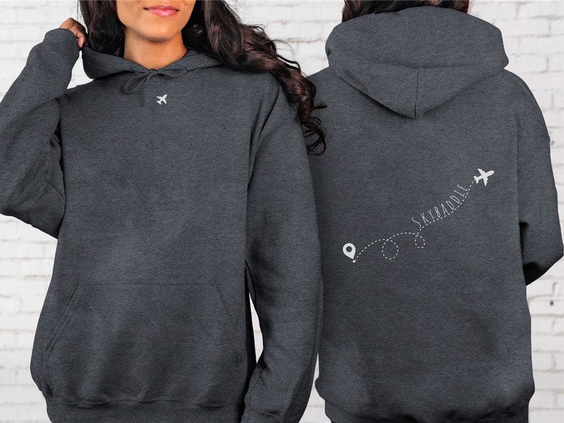 May include: A dark gray hoodie with a white airplane and the text "SKY&ADDLE" on the back. The text is written in a cursive font and is followed by a dotted line with a small airplane icon at the end.