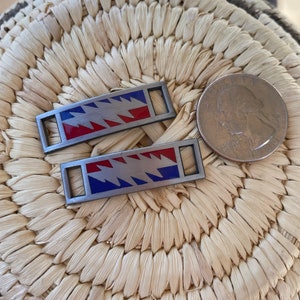 Puede incluir: Dos cordones de zapatos de metal plateado con un diseño de rayo rojo, blanco y azul. Los cordones están sobre una superficie tejida.