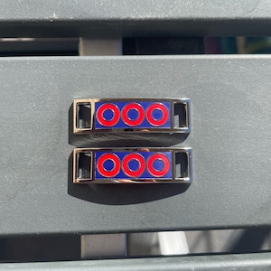 Peut inclure: Deux breloques de chaussures argentées avec trois cercles rouges et bleus sur chaque breloque.