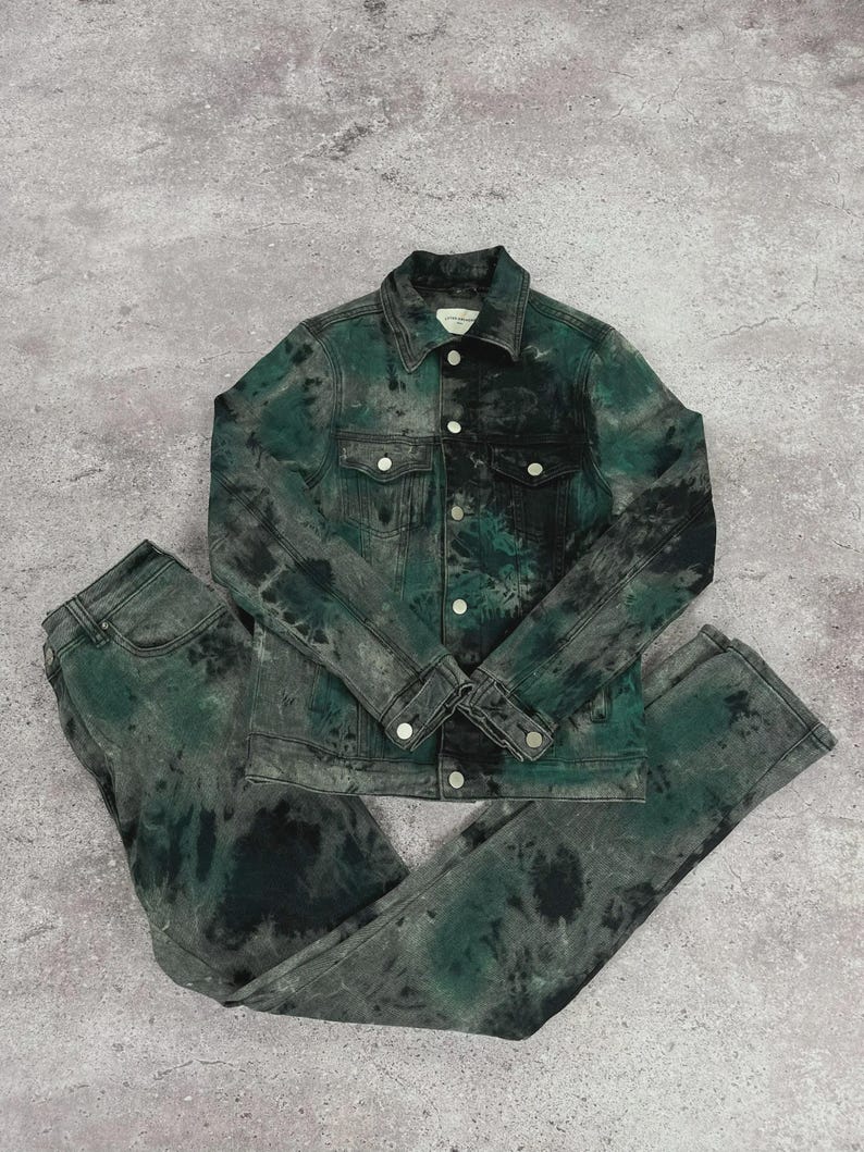 May include: A matching denim jacket and jeans set. The jacket has a button-up front and two chest pockets. The set is dyed in shades of green and black, creating a tie-dye effect. The jeans are straight-legged.
