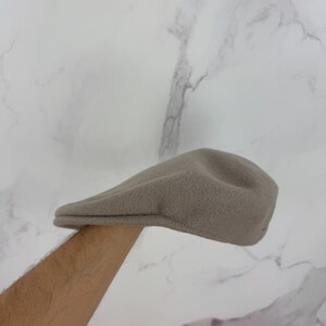 May include: A tan-colored, fleece newsboy cap. The hat has a rounded crown and a small, stiff brim. The cap is made of a soft, textured material. The hat is a classic style, suitable for various outfits.