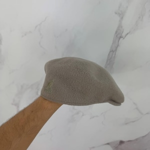 May include: A light gray Kangol beret with a textured, fuzzy surface. The beret features the Kangol logo embroidered in a darker gray on the side. This classic hat is a stylish accessory for any outfit.