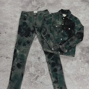 May include: A matching denim jacket and jeans set. The jacket has button closures and chest pockets. The jeans are a classic five-pocket design. Both pieces are dyed in a tie-dye pattern with black and green hues.