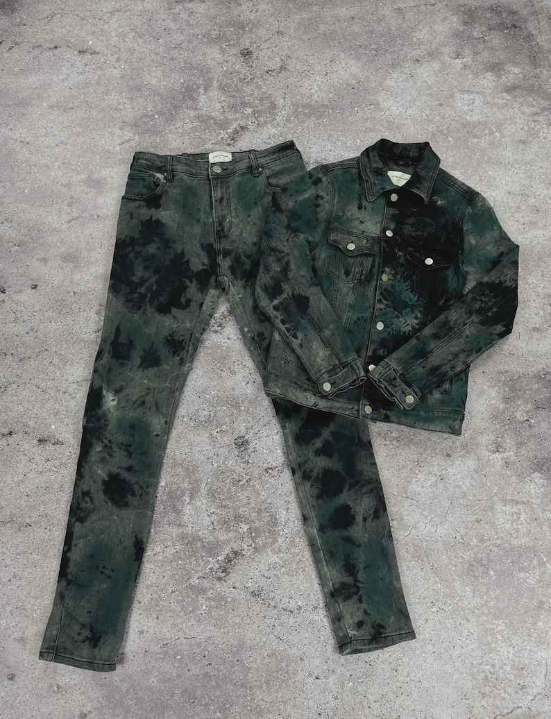 May include: A matching denim jacket and jeans set. The jacket has button closures and chest pockets. The jeans are a classic five-pocket design. Both pieces are dyed in a tie-dye pattern with black and green hues.
