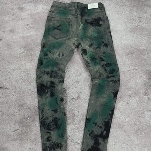 May include: Gray denim jeans with a tie-dye pattern in black and green. The jeans have a classic five-pocket design and a straight leg fit. The back pockets are visible, and a white tag is at the back.