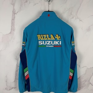 May include: A turquoise fleece jacket with a high collar and a red emblem. The back features the text "RIZLA SUZUKI" in gold and white, with a green, white, and red stripe. The sleeves have navy blue and multi-colored accents. A silver chain hangs above.